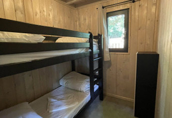 Et lille værelse i en lodge med køjesenge i mørkt træ, lyst træpanel på væggene og et lille vindue.