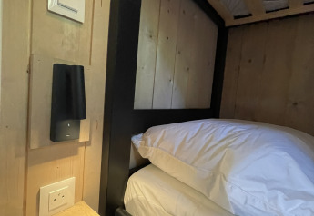 Close-up van een stapelbed naast een muur met stopcontact, klein plankje en leeslamp in een lodgekamer.