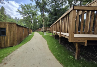Photo of a cozy lodge with wooden cabins and raised decks, set along a path surrounded by lush trees.