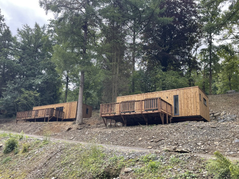 Zwei moderne Holzhütten auf einem Hang im Wald, ideal für einen ruhigen Urlaub in der Natur.