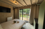 Gemütliches Schlafzimmer in einer Lodge mit Holzwänden, Doppelbett, TV und Blick auf Terrasse und Natur.