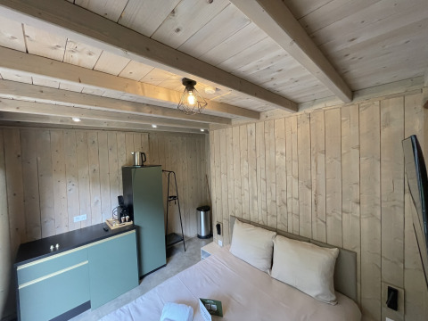 Sfeervolle lodgekamer met houten bekleding, tweepersoonsbed, kitchenette, koelkast en koffiezet.