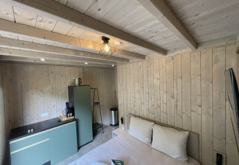 Et moderne lodgeværelse med trægulve, dobbeltseng, tekøkken, kaffemaskine og minimalistisk indretning.