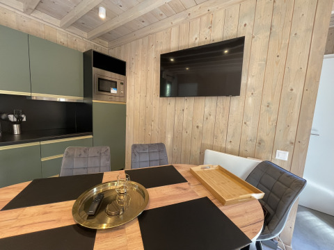 Modern lodge kitchen with wood panel walls, flat-screen TV, round dining table, and stylish chairs.