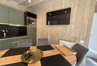 Modern lodge kitchen with wood panel walls, flat-screen TV, round dining table, and stylish chairs.