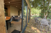 Innen- und Außenansicht einer Ecolodge im Hameau de la Semois, Belgien, mit Terrasse und Gartenmöbeln.
