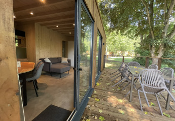 Innen- und Außenansicht einer Ecolodge im Hameau de la Semois, Belgien, mit Terrasse und Gartenmöbeln.