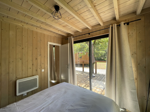 Innenansicht eines Schlafzimmers in einer Holzhütte mit großen Fenstern zur Terrasse im Grünen.