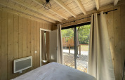 Interior view from a bedroom in a wooden lodge with large windows opening to a terrace and nature.