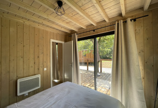 Interior view from a bedroom in a wooden lodge with large windows opening to a terrace and nature.