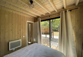 Innenansicht eines Schlafzimmers in einer Holzhütte mit großen Fenstern zur Terrasse im Grünen.