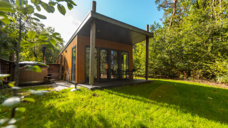 Wellness Lodge moderna con rivestimento in legno, veranda coperta e ampie vetrate nel verde della foresta.