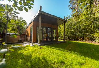 Wellness Lodge moderne en bois avec terrasse couverte, grandes baies vitrées et entourée de verdure luxuriante.