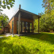 Wellness Lodge moderne en bois avec terrasse couverte, grandes baies vitrées et entourée de verdure luxuriante.