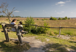 Une mère et son fils assis sur un banc en bois profitent de la vue à un hébergement glamping ensoleillé.