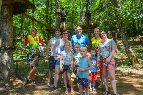 Groep mensen en kinderen poseren in een bosrijke omgeving bij een avonturenpark La Draille in Occitanie.