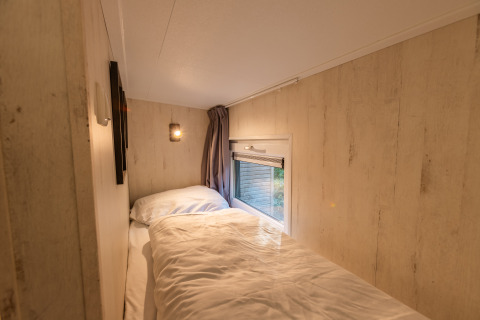 Accogliente zona notte nel Tiny Borg a Vakantiepark De Wiltzangh, Paesi Bassi, letto accanto alla finestra.