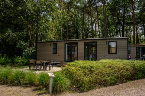 Ekstra luksus stacaravan på Familiepark Goolderheide i Belgien omgivet af skovtræer og havemøbler.