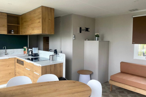 Modern mobile home kitchen and living area with wood cabinets at Extra Luxe Stacaravan, Familiepark Goolderheide, Belgium.