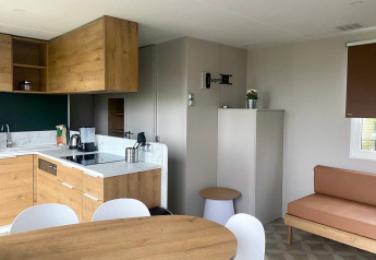 Modern mobile home kitchen and living area with wood cabinets at Extra Luxe Stacaravan, Familiepark Goolderheide, Belgium.