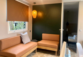 Modern mobile home living room with brown sofas, pendant lamp and window in Extra Luxe Stacaravan, Familiepark Goolderheide, Belgium.