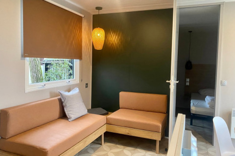 Modern mobile home living room with brown sofas, pendant lamp and window in Extra Luxe Stacaravan, Familiepark Goolderheide, Belgium.