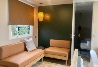 Moderne mobilhome stue med brune sofaer, hængelampe og vindue i Extra Luxe Stacaravan, Familiepark Goolderheide, Belgien.