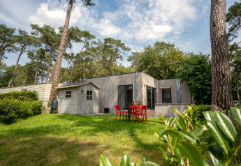 Chalet en Familiepark Goolderheide, Bélgica, rodeado de árboles y jardín con mesa y sillas exteriores.