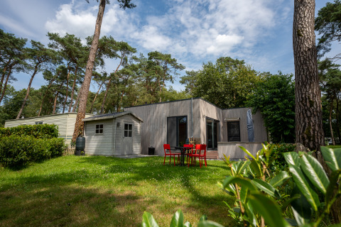 Chalet au Familiepark Goolderheide en Belgique entouré d’arbres avec espace repas extérieur dans le jardin.