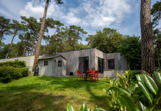 Chalet en Familiepark Goolderheide, Bélgica, rodeado de árboles y jardín con mesa y sillas exteriores.