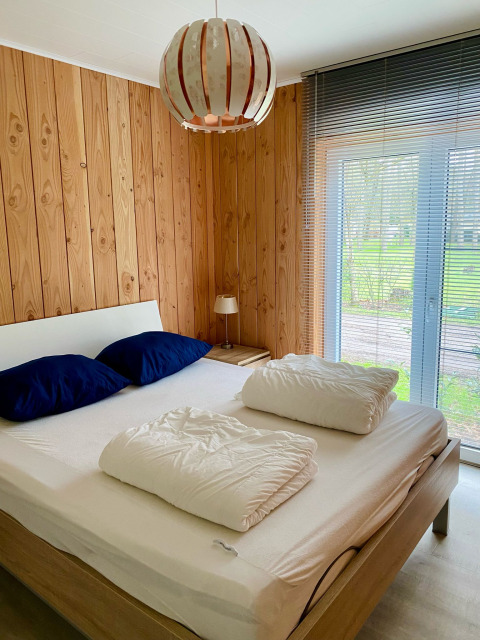 Bedroom with double bed, blue pillows, wooden panel walls, and garden view at Chalet in Familiepark Goolderheide, Belgium.