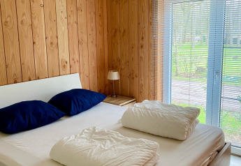 Chambre avec lit double, oreillers bleus, murs en bois et vue sur le jardin au Chalet du Familiepark Goolderheide, Belgique.