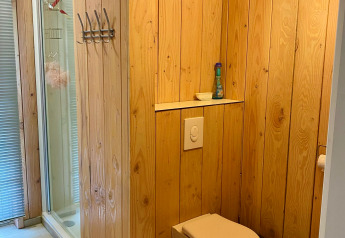 Baño en una cabaña con paneles de madera, inodoro de pared y ducha en Chalet de Familiepark Goolderheide.