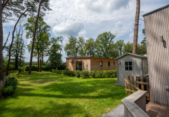 View of a green garden with a wooden chalet and shed at Familiepark Goolderheide in Belgium.