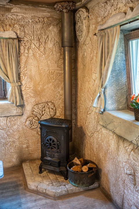 Coin chaleureux avec poêle à bois et bûches près d'une fenêtre au Hobbit huisje, Familiepark Goolderheide, Belgique.