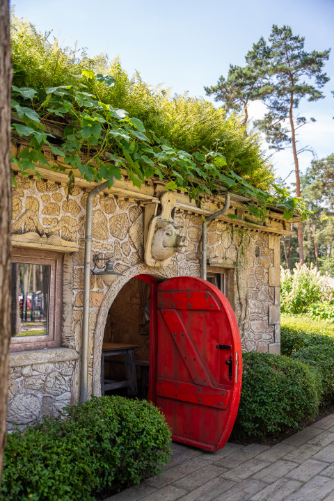 Charming stone cabin with red arched door and green roof at Hobbit huisje, Familiepark Goolderheide, Belgium.