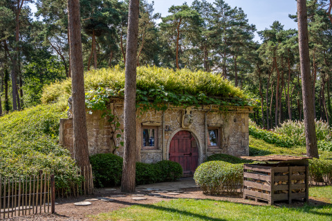 Hobbit huisje Hütte aus Stein mit bewachsenem Dach, eingebettet zwischen Bäumen und Grün im Wald.