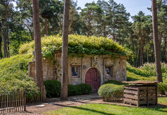 Hobbit huisje stone cottage with a green roof, nestled in a forest and surrounded by lush greenery.
