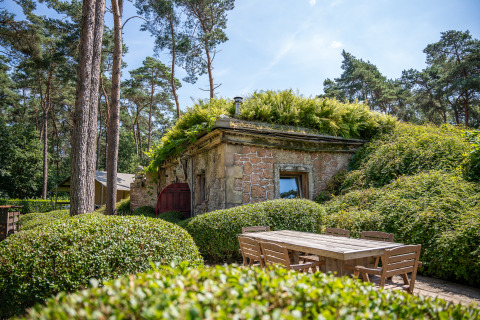 Hobbit-Haus mit bepflanztem Dach und Holzmöbeln vor dem Gebäude im Familiepark Goolderheide, Belgien.