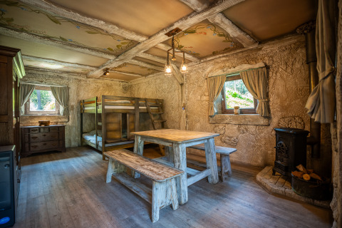 Innenaufnahme des Hobbit huisje: Gemütliche Holzhütte mit Etagenbett, Tisch und Kamin in Belgien.