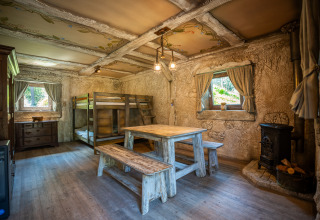 Interno del Hobbit huisje in Belgio, con letti a castello rustici, tavolo di legno e stufa accogliente.