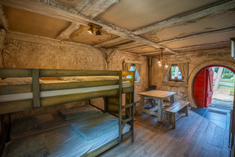 Interior of the Hobbit huisje cabin with bunk beds, wooden table, and a round red door at Familiepark Goolderheide.