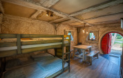 Interno della cabina Hobbit huisje con letti a castello, tavolo di legno e porta rotonda rossa a Familiepark Goolderheide.