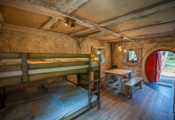 Innenraum der Hobbit huisje Hütte mit Etagenbetten, Holztisch und runder roter Tür im Familiepark Goolderheide.