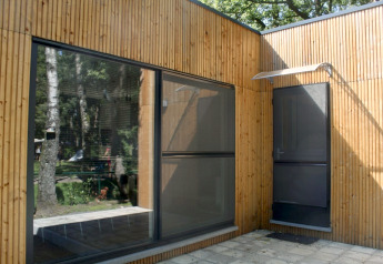 Fachada de un moderno chalet de madera con grandes ventanales en Familiepark Goolderheide, Bélgica.