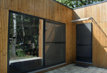 Fachada de un moderno chalet de madera con grandes ventanales en Familiepark Goolderheide, Bélgica.