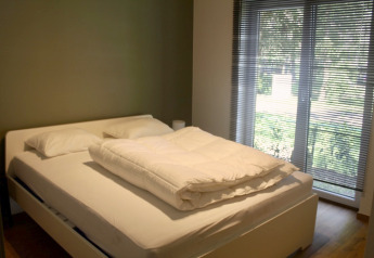 Dormitorio con cama doble, almohadas, edredón y grandes ventanas en un chalet de Familiepark Goolderheide, Bélgica.