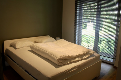 Dormitorio con cama doble, almohadas, edredón y grandes ventanas en un chalet de Familiepark Goolderheide, Bélgica.