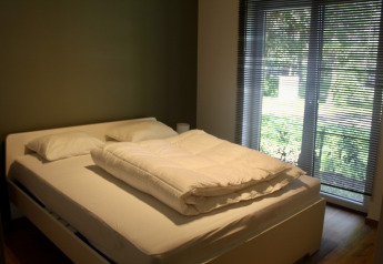 Chambre avec lit double, oreillers, couette et grandes fenêtres au Chalet du Familiepark Goolderheide en Belgique.