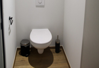 Inodoro moderno en un chalet de Familiepark Goolderheide, Bélgica, con suelo de madera y paredes blancas.